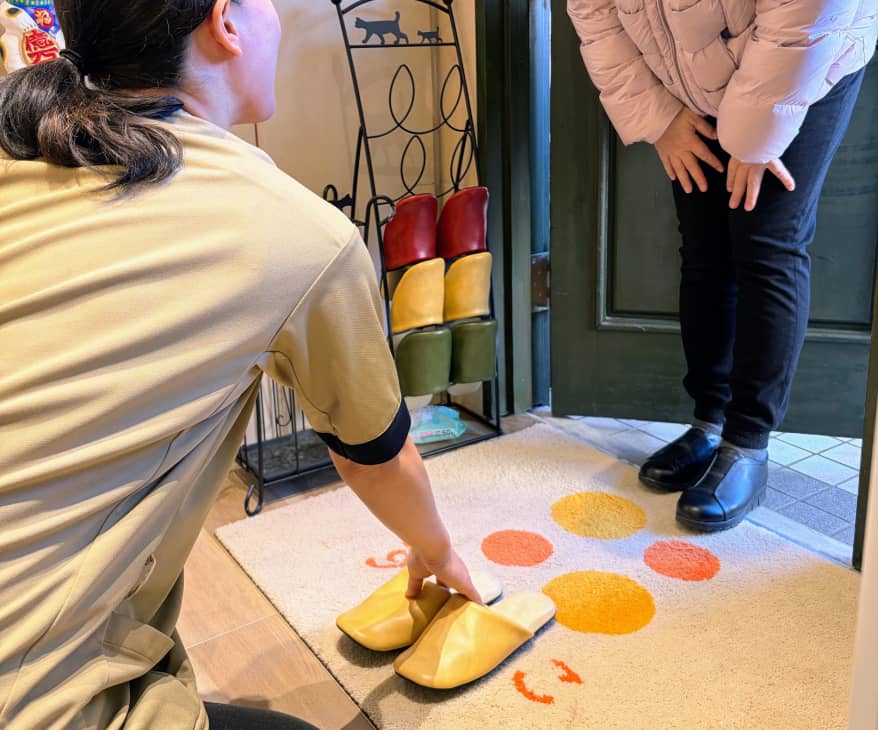 来店者にスリッパを差し出して丁寧に迎えるスタッフの様子