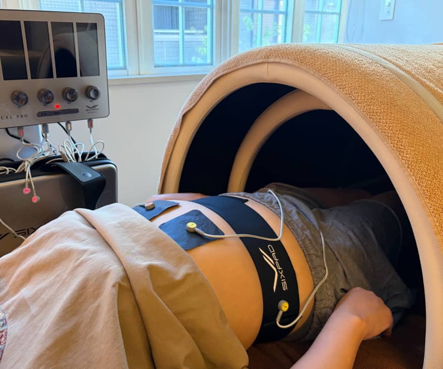 リハビリ中の患者が腰に通電パッドを装着し、温熱ドームに入っている治療風景